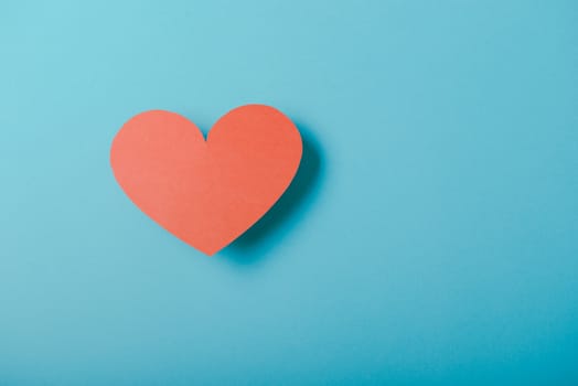 Red paper Valentines Day heart against a blue background