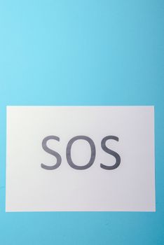 Word SOS written on white paper. Blue background