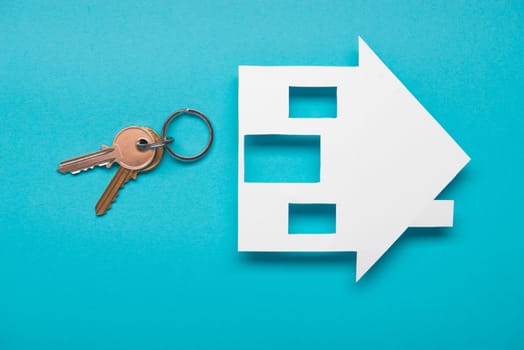 Silver key with house figure on blue background. Top view.