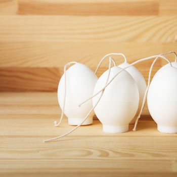 Decorative Handmade candles in the shape of eggs ready for painting and decorating for the holiday. White candles on wood background with copy-space. Candle lit. Happy Easter