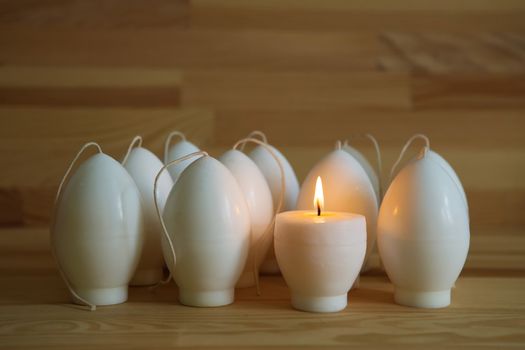 Decorative Handmade candles in the shape of eggs ready for painting and decorating for the holiday. White candles on wood background with copy-space. Candle lit. Happy Easter