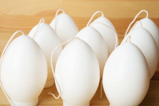 Decorative Handmade candles in the shape of eggs ready for painting and decorating for the holiday. White candles on wood background with copy-space. Candle lit. Happy Easter