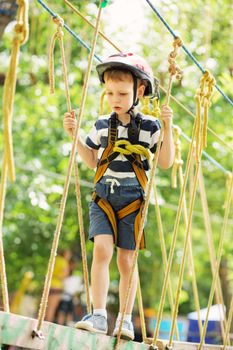 Kids climbing in adventure park. Boy enjoys climbing in the ropes course adventure. Child climbing high wire park. Happy boys playing at adventure park, holding ropes and climbing wooden stairs.