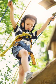 Kids climbing in adventure park. Boy enjoys climbing in the ropes course adventure. Child climbing high wire park. Happy boys playing at adventure park, holding ropes and climbing wooden stairs.