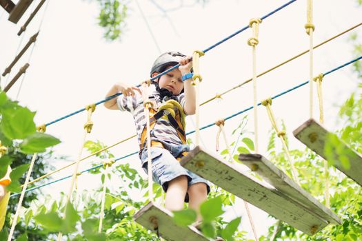 Kids climbing in adventure park. Boy enjoys climbing in the ropes course adventure. Child climbing high wire park. Happy boys playing at adventure park, holding ropes and climbing wooden stairs.