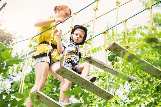 Kids climbing in adventure park. Boy enjoys climbing in the ropes course adventure. Child climbing high wire park. Happy boys playing at adventure park, holding ropes and climbing wooden stairs.