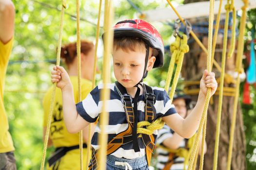 Kids climbing in adventure park. Boy enjoys climbing in the ropes course adventure. Child climbing high wire park. Happy boys playing at adventure park, holding ropes and climbing wooden stairs.