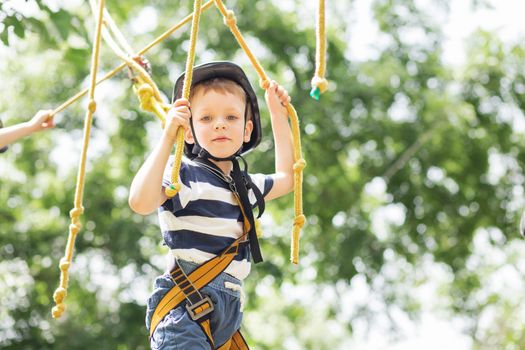 Kids climbing in adventure park. Boy enjoys climbing in the ropes course adventure. Child climbing high wire park. Happy boys playing at adventure park, holding ropes and climbing wooden stairs.