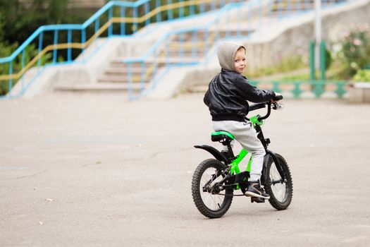 portrait of adorable little urban boy wearing black leather jacket. City style. Urban kids. The boy learns to ride a bike. Child driving a bicycle.