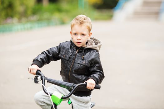 portrait of adorable little urban boy wearing black leather jacket. City style. Urban kids. The boy learns to ride a bike. Child driving a bicycle.