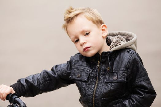 portrait of adorable little urban boy wearing black leather jacket. City style. Urban kids. The boy learns to ride a bike. Child driving a bicycle.