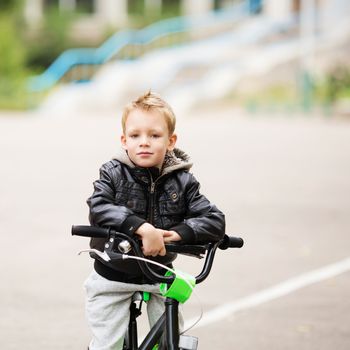 portrait of adorable little urban boy wearing black leather jacket. City style. Urban kids. The boy learns to ride a bike. Child driving a bicycle.