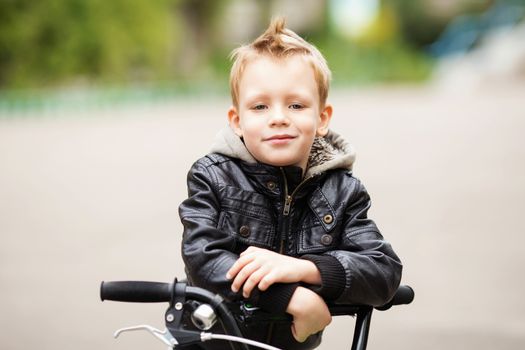 portrait of adorable little urban boy wearing black leather jacket. City style. Urban kids. The boy learns to ride a bike. Child driving a bicycle.