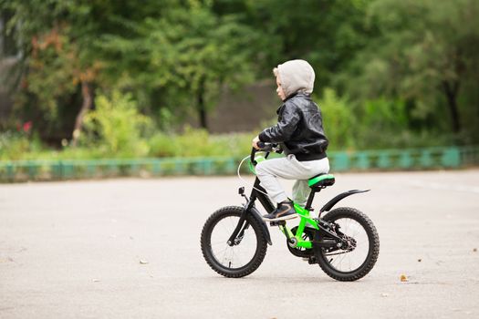 portrait of adorable little urban boy wearing black leather jacket. City style. Urban kids. The boy learns to ride a bike. Child driving a bicycle.