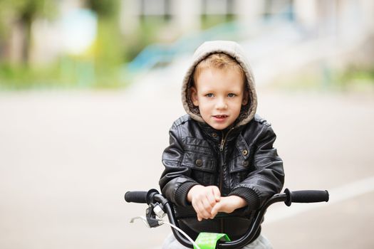 portrait of adorable little urban boy wearing black leather jacket. City style. Urban kids. The boy learns to ride a bike. Child driving a bicycle.