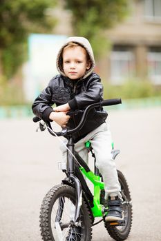 portrait of adorable little urban boy wearing black leather jacket. City style. Urban kids. The boy learns to ride a bike. Child driving a bicycle.