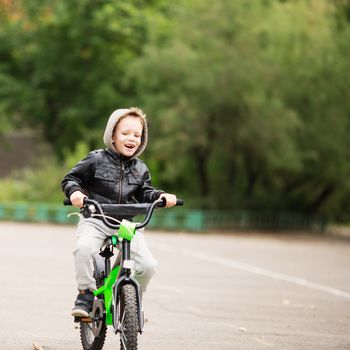 portrait of adorable little urban boy wearing black leather jacket. City style. Urban kids. The boy learns to ride a bike. Child driving a bicycle.