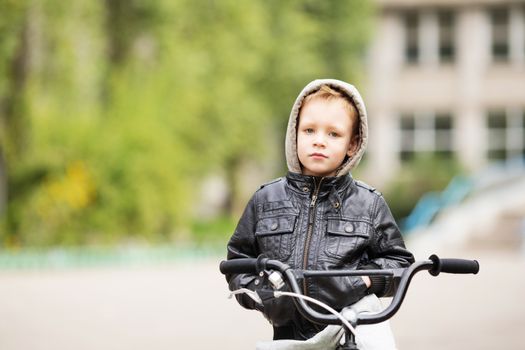 portrait of adorable little urban boy wearing black leather jacket. City style. Urban kids. The boy learns to ride a bike. Child driving a bicycle.