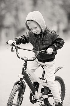 portrait of adorable little urban boy wearing black leather jacket. City style. Urban kids. The boy learns to ride a bike. Child driving a bicycle.