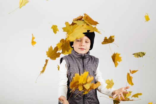 Portrait of happy joyful beautiful little boy against white background. Child holding a yellow maple leaves. Kid throws up a autumn yellowed foliage