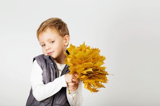 Portrait of happy joyful beautiful little boy against white background. Child holding a yellow maple leaves. Kid throws up a autumn yellowed foliage
