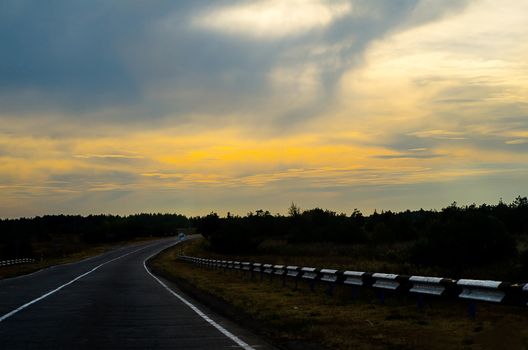 Long highway at sunset. Trees, grass, clouds. Anyone. Horizontal photo