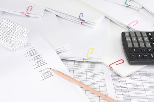 Pencil on earnings statement have blur house and calculator on stack paperwork of report and receipt with colorful paperclip as background.