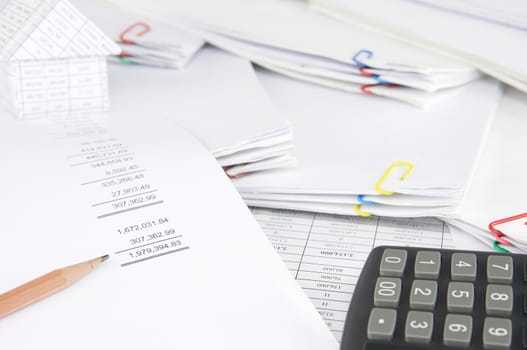 Brown pencil on earnings statement have blur house and calculator on stack paperwork of report and receipt with colorful paperclip as background.