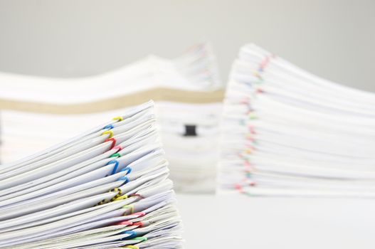 Pile overload paperwork of receipt and report with colorful paperclip have blur pile document as background on white table.