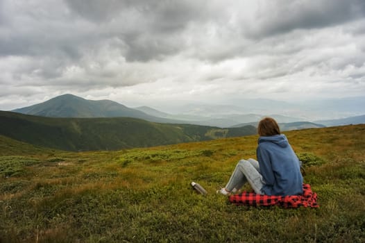Female person sitting and enjoying beautiful view of mountain landscape on a cloudy day