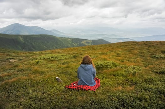 Girl sitting and enjoying beautiful view of mountain landscape on a cloudy day