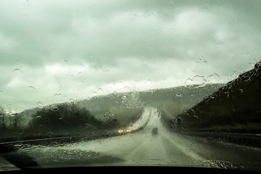 View from the car front seat on the long road ahead during the rain, raindrops on front window