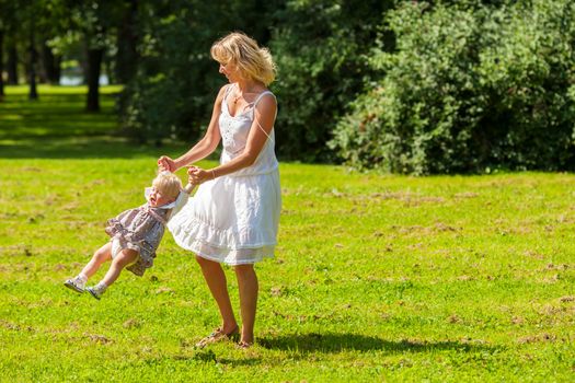 Happy mother spinning with one year daughter outdoors