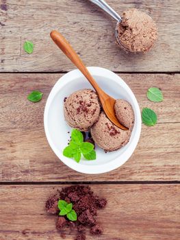 Chocolate ice cream in white bowl with fresh peppermint leaves and  ice cream scoop setup on shabby wooden background  . Summer and Dessert menu concept .