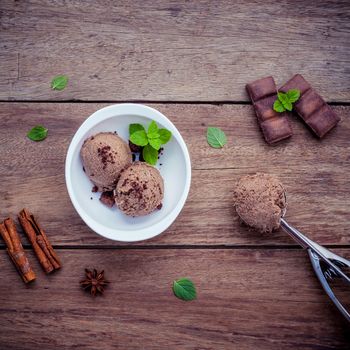 Chocolate ice cream in white bowl with fresh peppermint leaves and dark chocolate bars setup on shabby wooden background  . Summer and Dessert menu concept .