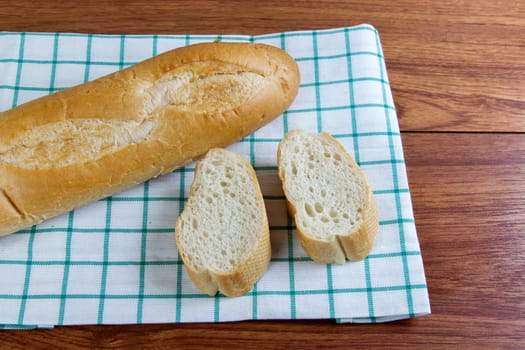 French bread baguette cut on white fabric with wooden board