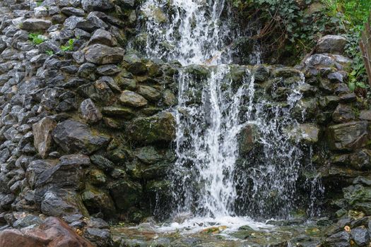 Small waterfall, cascade flowing over mossy boulders in a botanical garden.