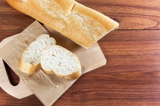 French bread baguette cut on brown paper with wooden board