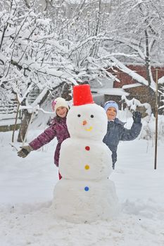 Happy children building snowman in garden