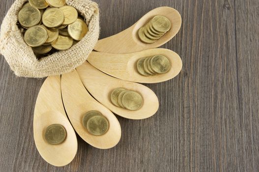 Top view of gold coins in wooden spoon with brown sack of gold coins on wood background.