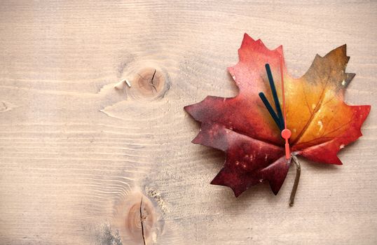 Autumn leaf with clock hands on top of a wooden background