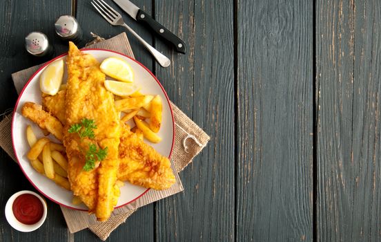 Two pieces of battered fish on a plate with chips on a wooden table with space 