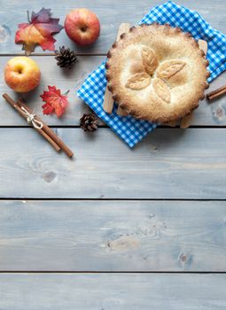 Apple pie with fruit ingredients autumn leaves and cinammon sticks on a wooden table