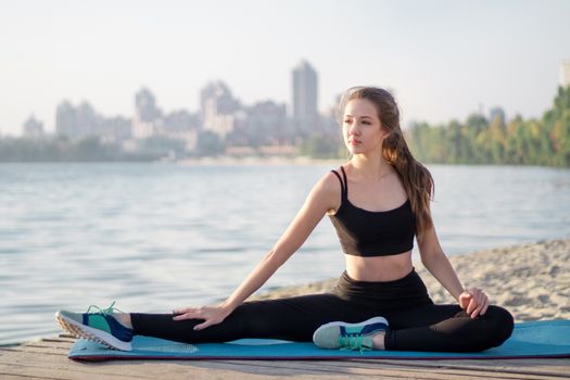 Young pretty slim fitness sporty woman rests and poses outdoor during training workout exercises at river coast in the morning