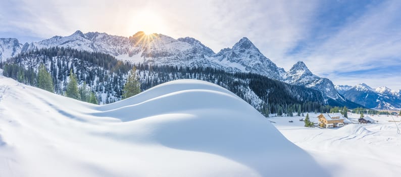 Winter panorama with an Austrian village, the Alps mountains and big piles of snow, on a sunny day of December.