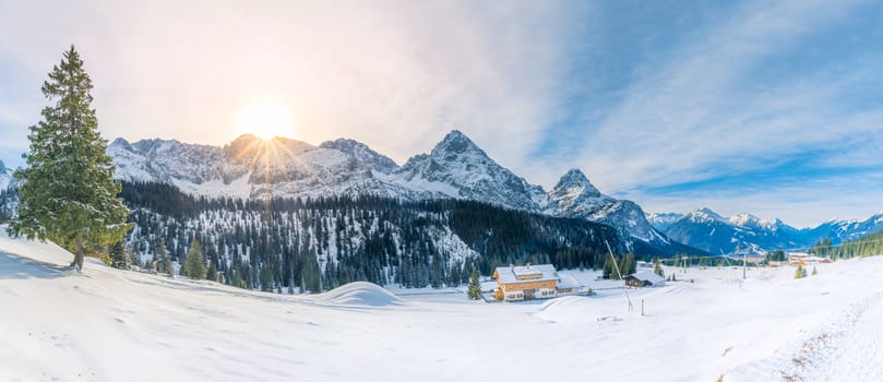 Winter fairytale scenery with a small Austrian village, evergreen fir trees and the Alps covered in snow, on a sunny day of December.