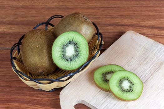 fresh kiwi  fruits and slices of kiwi fruit in basket on wood