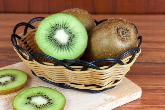 fresh kiwi  fruits and slices of kiwi fruit in basket on wood