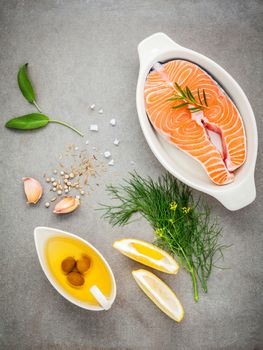 Raw salmon fillet in the white bowl with ingredients olive oil ,sea salt, and herbs  fennel ,sage ,rosemary ,garlic ,pepper and lemon for cooking on concrete background .