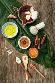 Green leaves with nature spa ingredients turmeric,herbal compress ball,dried indian bael ,cinnamon powder ,cinnamon sticks ,aromatic oil ,star anise and sea salt on rustic background.